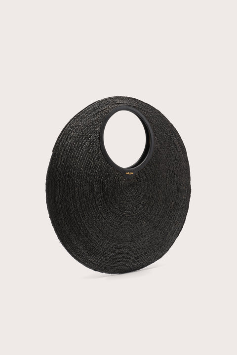 Side angle of an oversized black woven circular  handbag on a light beige background