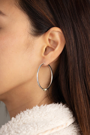 A woman wearing a sterling silver hoop earring with three yellow gold annulets.