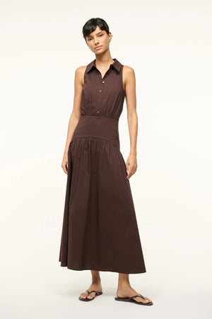 Woman wearing a brown collared, sleeveless dress that features a curved yoke detail at the hip, paired with brown sandals.