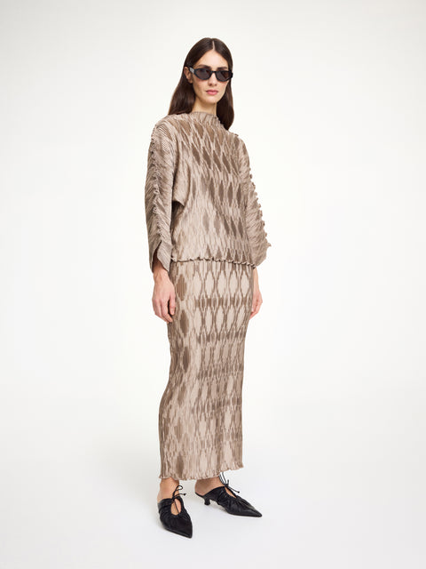 Side-facing woman wearing a textured beige top that features wide sleeves and a boatneck neckline, paired with a matching skirt.