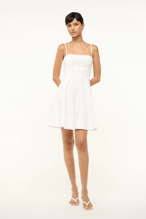 Woman wearing a white poplin mini dress that features a square neck with spaghetti straps, a fitted bodice with corset-style paneling, and a full skirt.