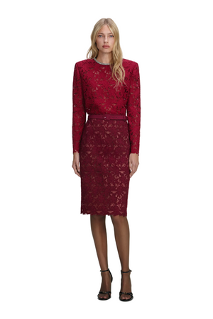 Woman wearing a red lace top with embellishment on the and matching midi skirt on a white background