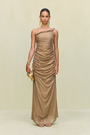 Woman wearing a gold metallic gown that features a hand rolled, one-shoulder neckline and intricate ruched draping throughout the body, paired with gold heels and accessories.