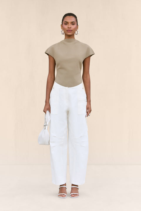 Woman wearing a tan knit shirt that features a mock neck and structures cap sleeves, paired with white cargo pants.