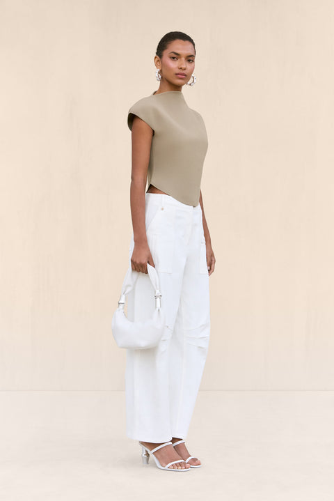 Side-facing woman wearing a tan knit shirt that features a mock neck and structures cap sleeves, paired with white cargo pants.