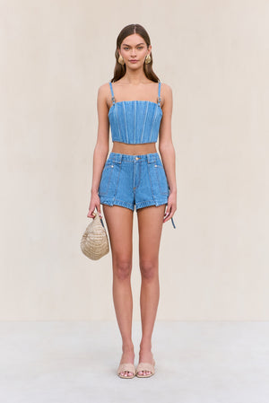 Woman wearing a blue denim corset with matching cargo denim shorts, paired with a tan handbag and nude sandals.
