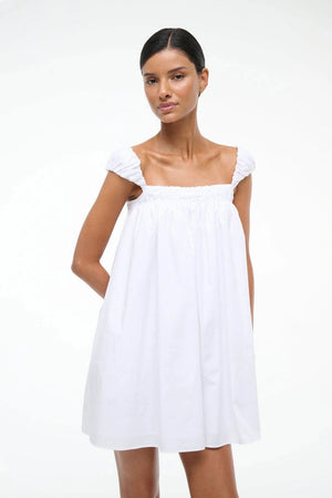 Woman wearing a white mini babydoll dress that features puffed cap sleeves.