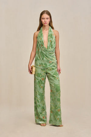 Woman wearing a green wide leg pant with velvet and silk burnout patterns and gold details, paired with a matching top.