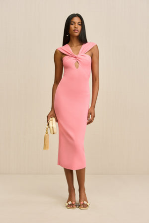 Woman wearing a versatile pink, knit midi dress that features a keyhole cutout and convertible neckline, pictured here styles with both straps over the shoulders, paired with a cream clutch and heels.