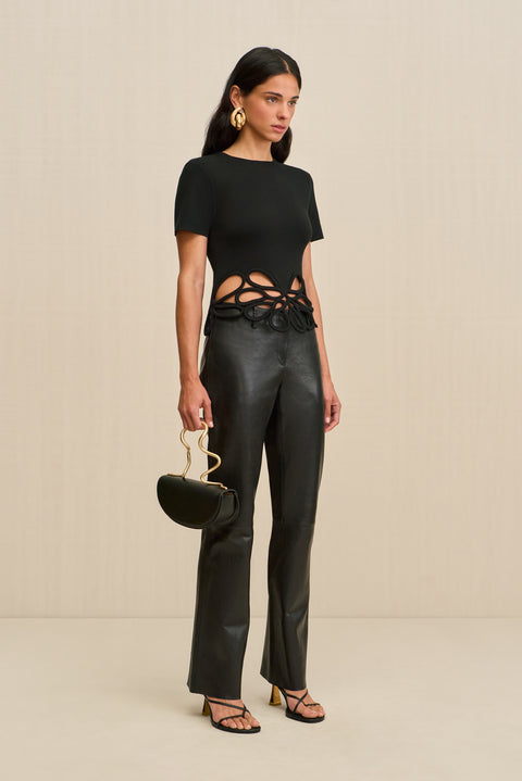 Side-facing woman wearing a black, knit t-shirt that features floral cutouts at the bottom hem, paired with black pants and black accessories.