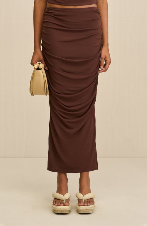 Close up of a woman wearing a brown fitted, stretchy maxi skirt that features ruching down the side seams.