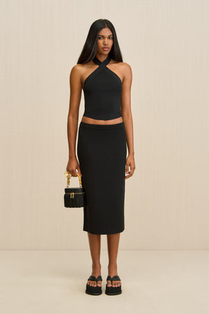 Woman wearing a black halter top and pencil skirt with a beige background