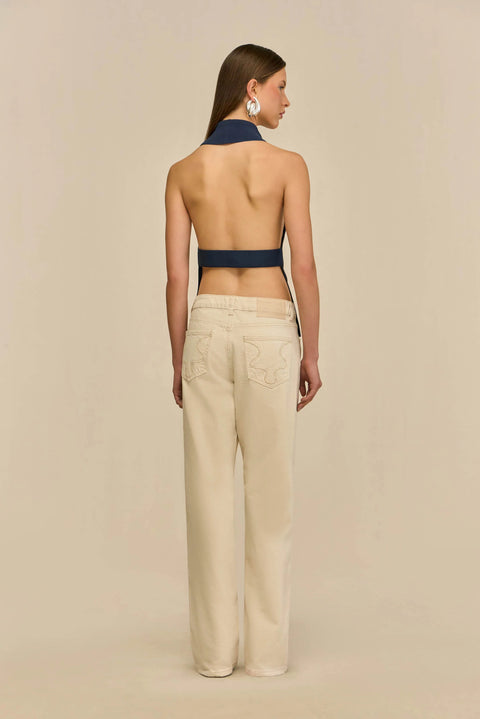 Back-facing shot of woman wearing a navy sleeveless top and beige pants on a beige background