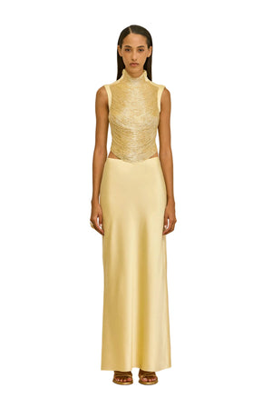 Woman wearing a gold beaded sleeveless top and long skirt against a beige background