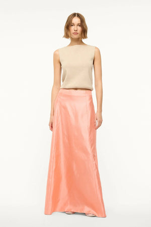 Woman wearing a pink silk, Aline, maxi skirt that features a back zipper and sits at the natural waist, paired with a tan sweater vest.