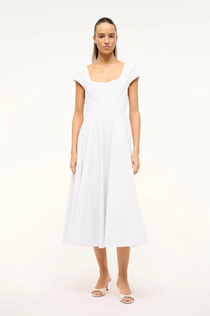 Woman wearing a white midi dress that features cap sleeves, a square neck, corset styles paneling, and an A-line skirt, paired with white heels.