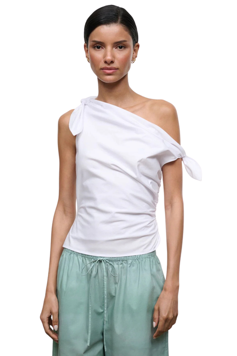 A model wearing a white asymmetrical one-shoulder tie-front top and sage green drawstring pants, photographed against a plain white background.