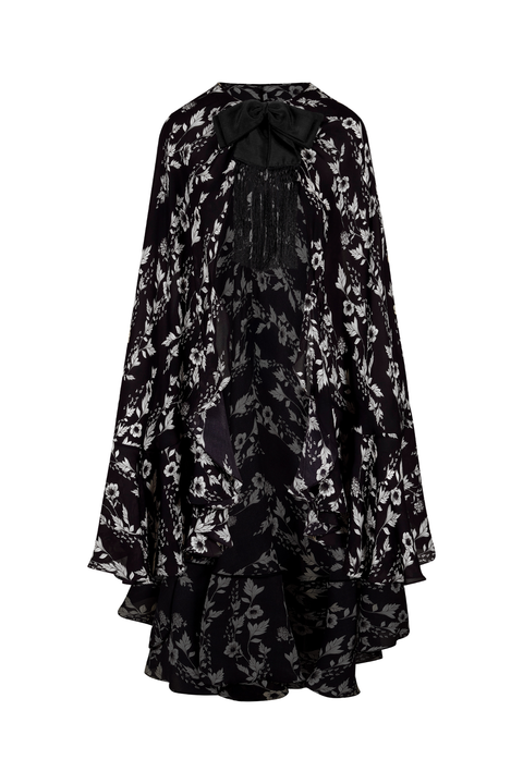A black and white floral lace cape-style top with a high-low ruffled hem and long sleeve shown against a plain white background.