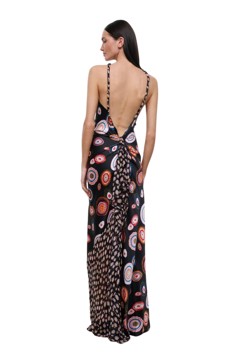 A woman modeling a black maxi dress with a colorful circular print, shown from the back against a plain white background.