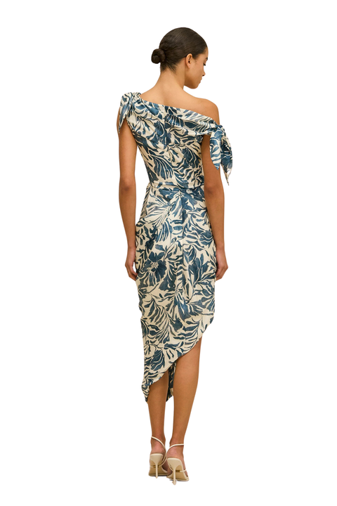A woman modeling a one-shoulder midi dress with a blue and beige tropical leaf print, shown from the back against a plain white background.