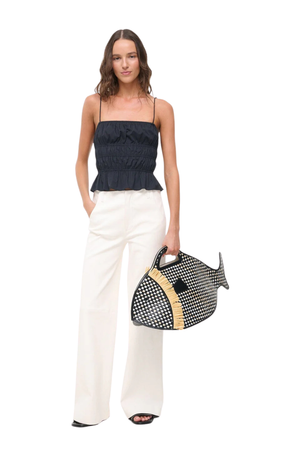 A woman wearing a black ruched cami with a pair of white pants and a patterned fish bag