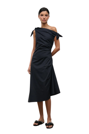 A model wearing a black off-the-shoulder midi dress with a ruched bodice and tie details, paired with black slide sandals, set against a plain white background.
