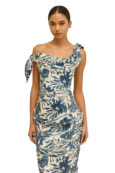A woman modeling a one-shoulder bodycon dress with a blue and cream floral print against a plain white background.
