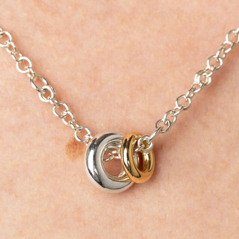 Close up of a woman wearing a Spinelli Kilcollin Gravity necklace with a sterling silver chain and a sterling silver annulet and a smaller yellow gold annulet.