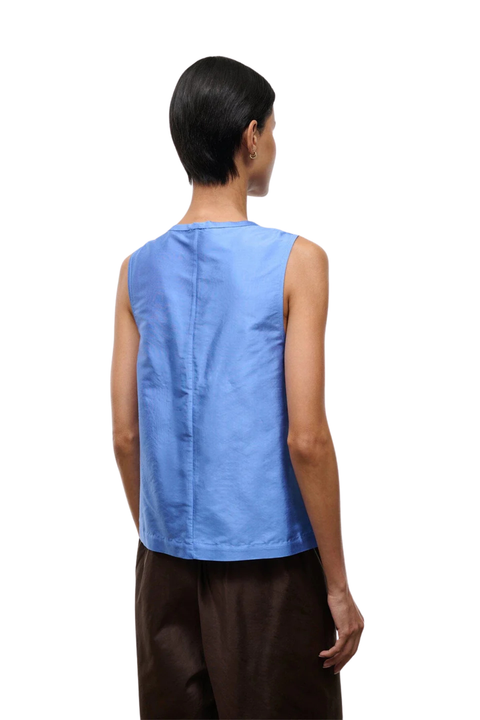 A model shown from the back wearing a sleeveless light blue top and dark brown pants against a plain white background.