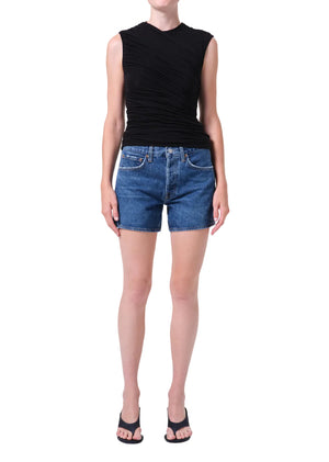 Person wearing a black sleeveless top and blue, high-rise denim shorts on a white background posing from the front