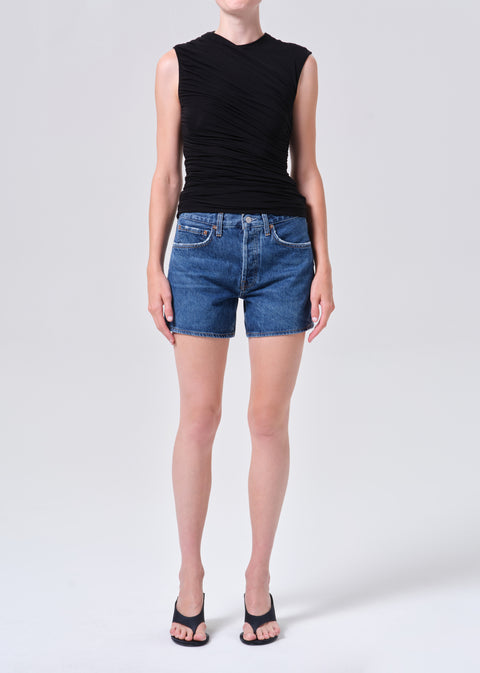 Person wearing a black sleeveless top and blue, high-rise denim shorts on a white background posing from the front