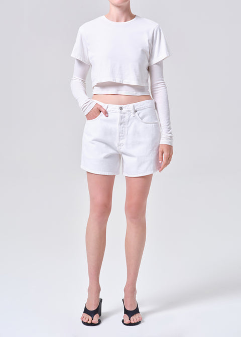 Person wearing a white long-sleeve crop top and white, high-rise denim shorts on a white background from the front