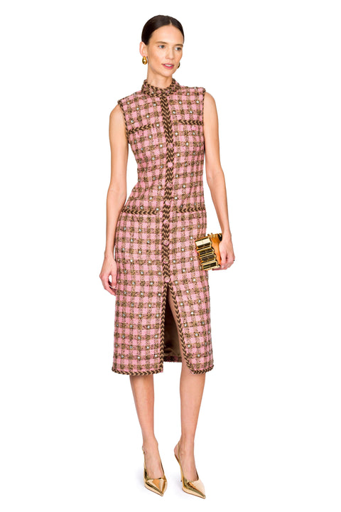 Woman posing in a pink and brown check patterned dress with a gold clutch on a white background