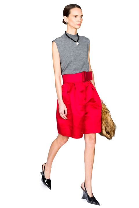 Woman walking to the right wearing a gray sleeveless top and red belted wide leg shorts and black heels with a white background