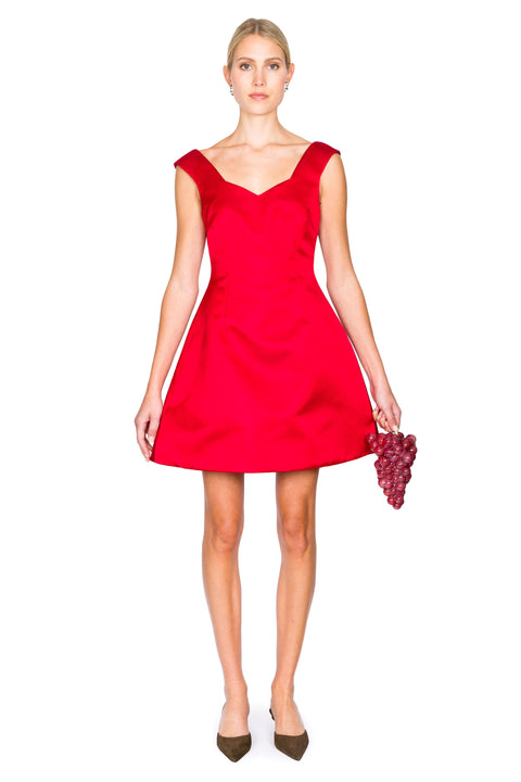 Woman wearing a red mini dress with sweetheart neckline holding a grapes clutch on a white background