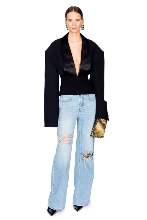 Woman posing, wearing a black long sleeve deep v-neck top and light blue jeans with distressing on a white background