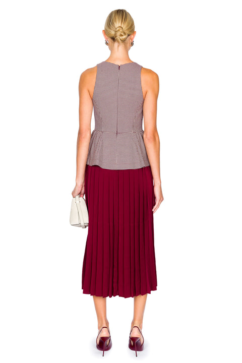 Back of woman wearing a sleeveless patterned top and pleated red skirt dress on a white background