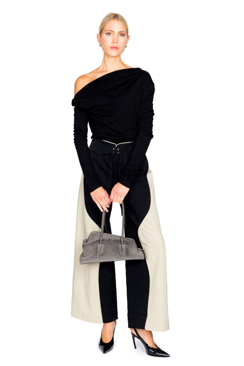 Woman poses wearing a black long sleeve top and wide leg pants holding a gray handbag on a white background