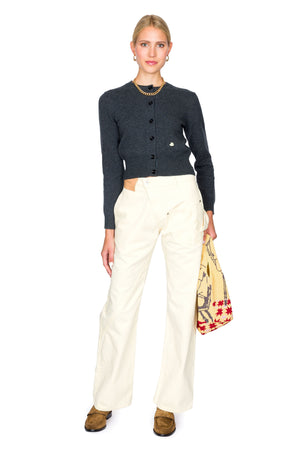 Woman wearing a dark grey cardigan, yellow denim, and brown shoes on a white background