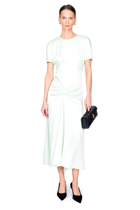 Woman wearing a light green midi dress holding a black clutch on a white background