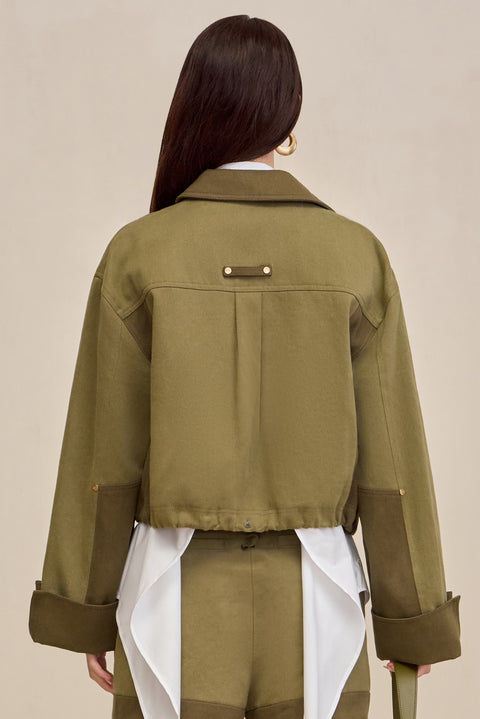 Back-facing woman wearing a two-tone green cropped barn-style jacket over a white button down and matching pants.