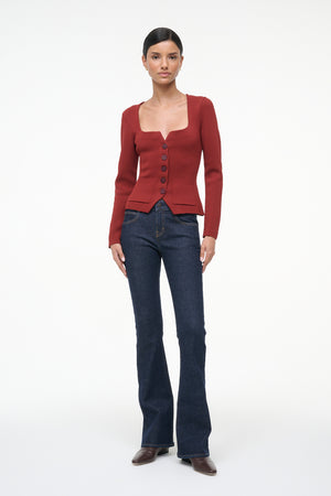 Woman wearing a red cardigan and blue jeans on a white background