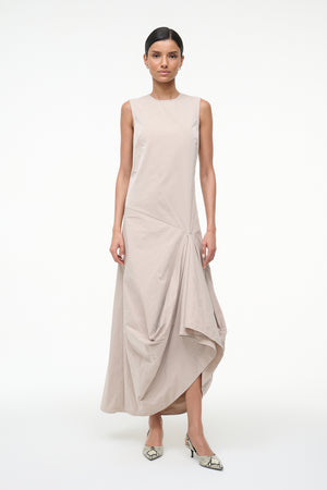 Woman wearing a beige sleeveless asymmetrical dress on a white background