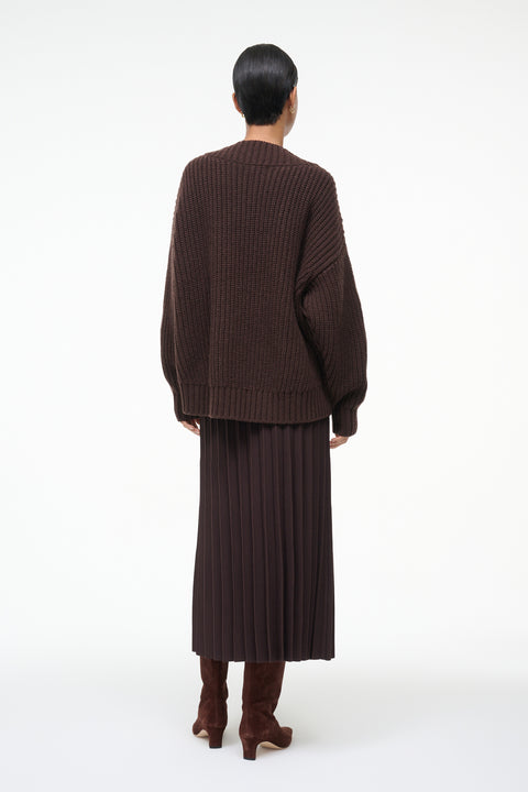 Person wearing a brown ribbed sweater and skirt set on a white background