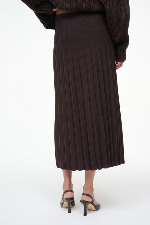 Person wearing a dark brown pleated skirt on a white background