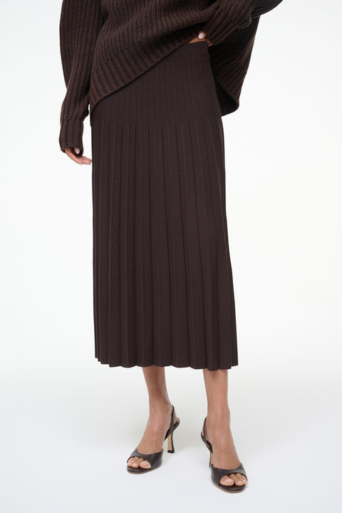 Person wearing a brown pleated skirt and sweater on a white background