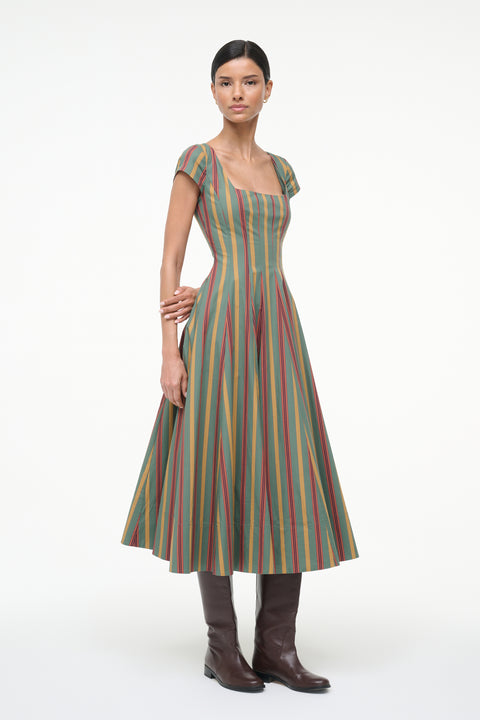 Side-facing woman wearing a green, red, and yellow striped midi dress with cap sleeves and a square neck with brown boots.