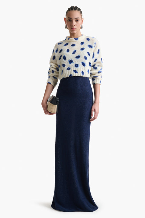Woman wears white cropped long sleeve sweater with blue smudge kisses print and navy maxi skirt.