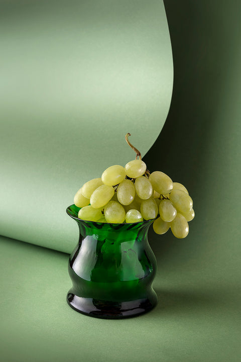 Green glass candle with green grapes on top of it with green backdrop.