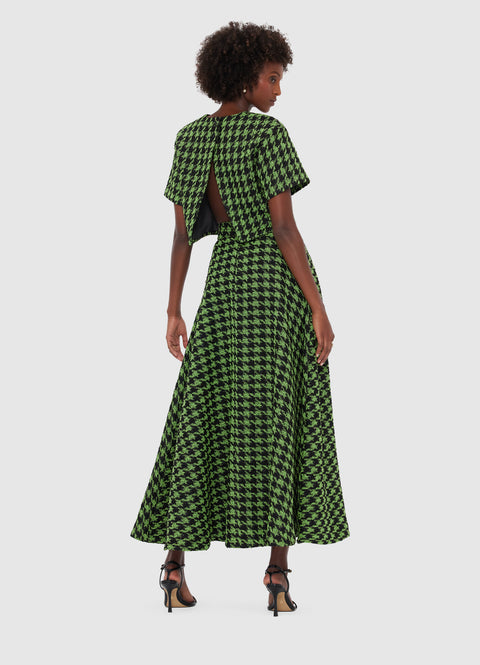 Back view of a woman wearing a green and black houndstooth tweed short sleeve crop top that has an open back and matching A-line maxi skirt, paired with black heels.